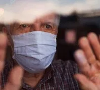 Old man looking out window with mask on